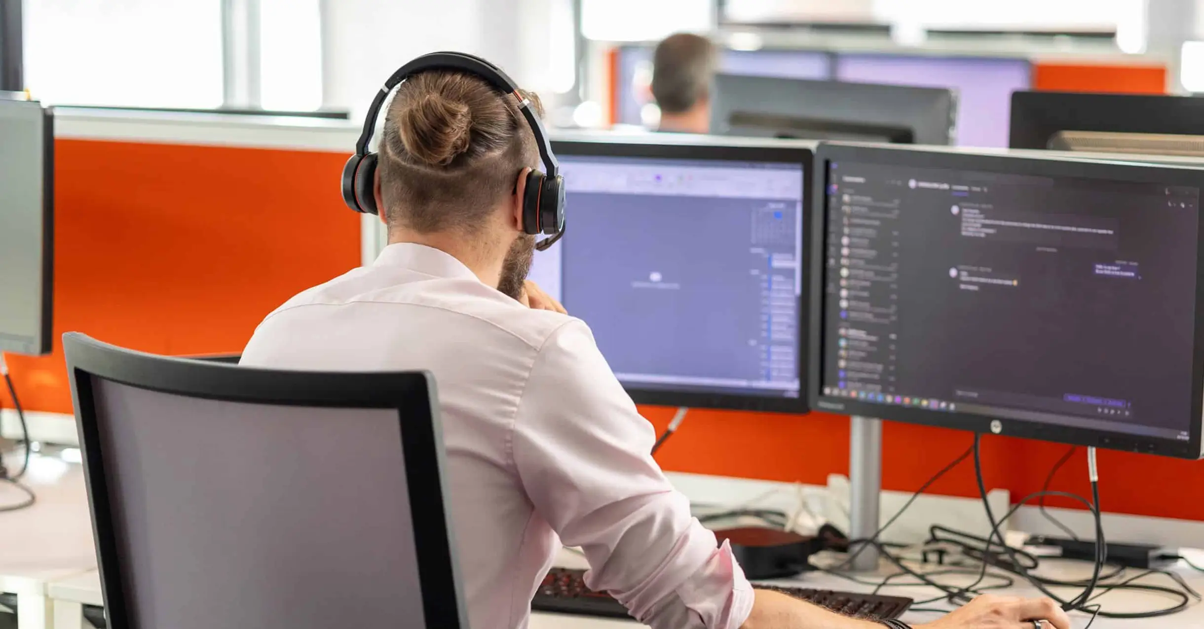Homme à son bureau face à deux écrans informatiques.